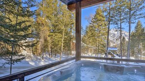 Un jacuzzi con terraza de madera y vistas a árboles y montañas nevadas.