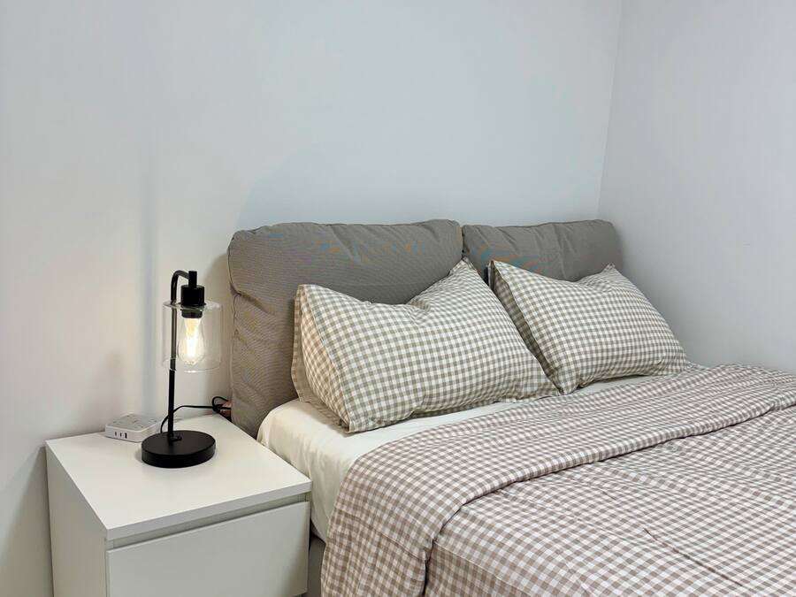 Un dormitorio ordenado con cama, almohadas, una mesita de noche y una lámpara.
