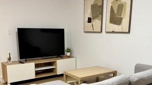 A modern living room with a flat-screen TV, a sofa, a coffee table, and two framed artworks on the wall. - Levida Living - Cozy 2 Bedroom Suite at the Heart of Langley (Langley)
