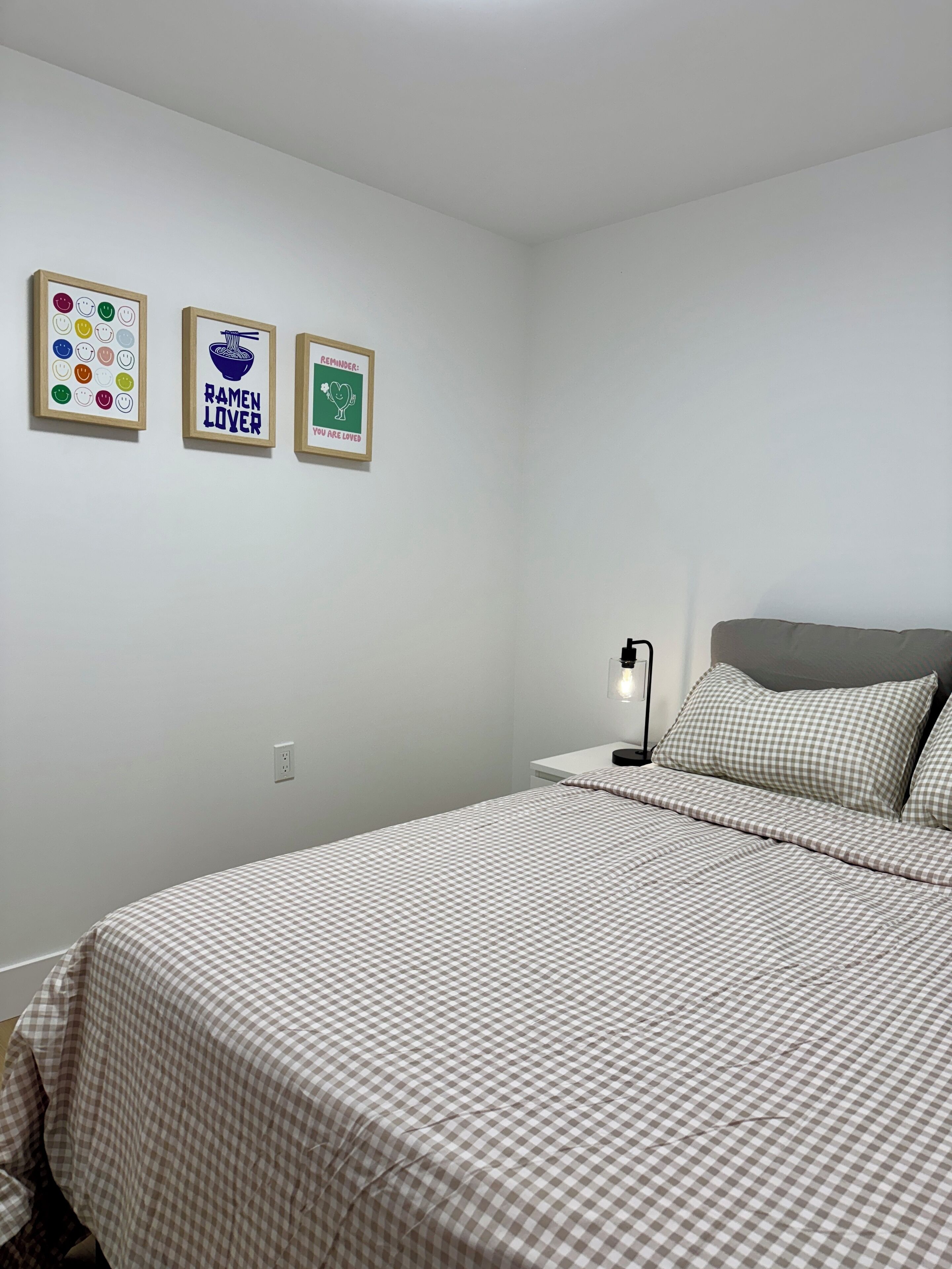 A bedroom with a bed, a bedside table, and three framed pictures on the wall.