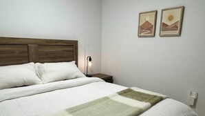 A neatly made bed with a checkered blanket, a wooden headboard, and two wall-mounted pictures depicting landscapes. - Levida Living - Cozy 2 Bedroom Suite at the Heart of Langley (Langley)