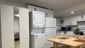 A modern kitchen with white appliances, a dining table with chairs, and a view into a bedroom. - Levida Living - Cozy 2 Bedroom Suite at the Heart of Langley (Langley)
