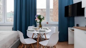 Ein gemütlicher Raum mit Bett, Esstisch mit Stühlen, Fernseher und einem Fenster mit Vorhängen.