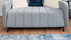 Ein modernes Wohnzimmer mit einem grauen Sofa, einem blauen Kissen und einem weißen, flauschigen Kissen. Ein gerahmtes Bild hängt über dem Sofa an der Wand.