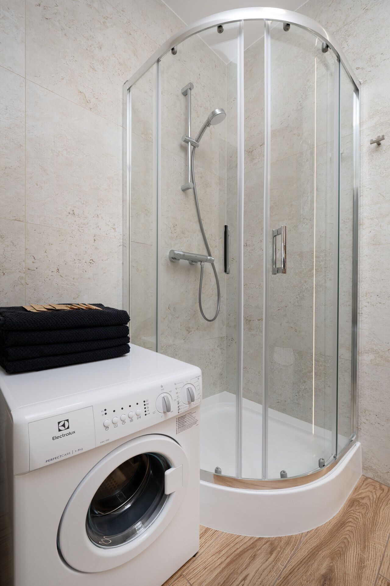 Un baño moderno con ducha envuelta en vidrio, lavadora blanca y toallas dobladas con cuidado.
