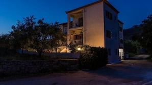 A two-story building with a balcony on the upper floor, surrounded by trees and a stone wall. - Lefkis apartments & studios (West Mani)