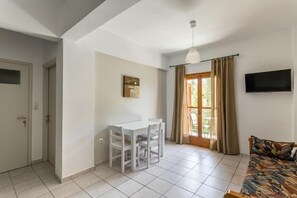 Um quarto com uma mesa de jantar e cadeiras, um sofá, uma televisão e uma janela com cortinas.