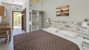 A bedroom with a large bed, a wooden headboard, a painting on the wall, and a view of the outdoors. - Lefkis apartments & studios (West Mani)