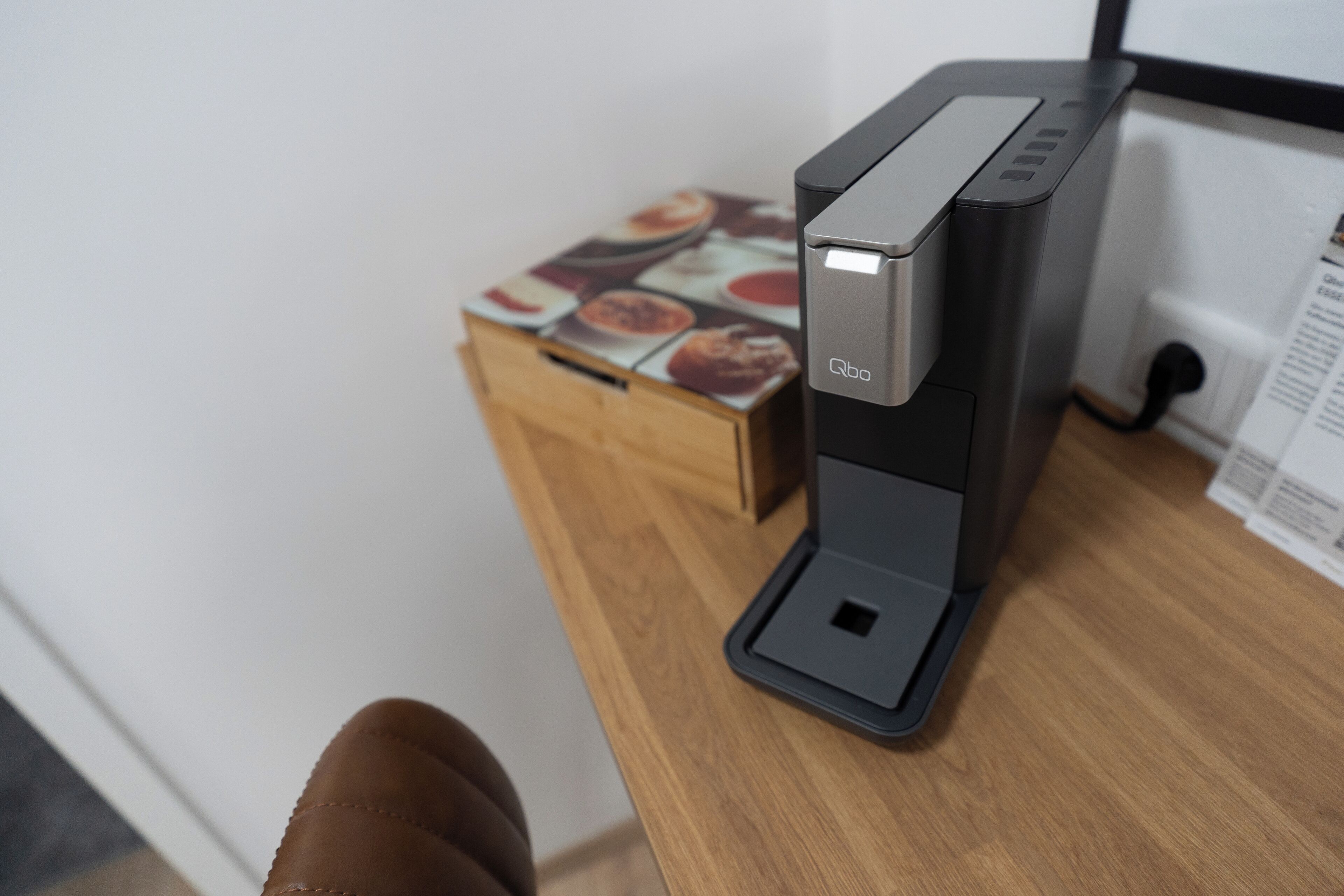 A coffee machine on a wooden table with a box of coffee pods in the background.