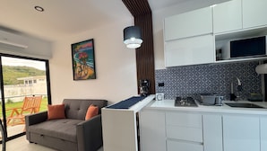 Cozinha moderna com armários brancos, fogão embutido e uma grande janela com vista para uma varanda.