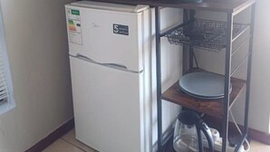 A compact kitchenette with a white refrigerator, a black microwave, and a small shelf with two rolls of paper towels. - Cloud 9 Room 6 King Bed & Stunning Views (Cape Town)