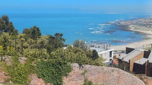 A coastal view with a beach, ocean, and a cityscape in the background. - Cloud 9 Room 6 King Bed & Stunning Views (Cape Town)