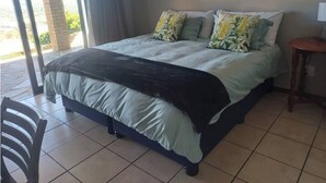 A bedroom with a bed, pillows, a chair, and a small table. - Cloud 9 Room 6 King Bed & Stunning Views (Cape Town)