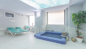 Een spa kamer met een klein zwembad, twee lounge stoelen, een plafond met wolken motief, en een potplant.