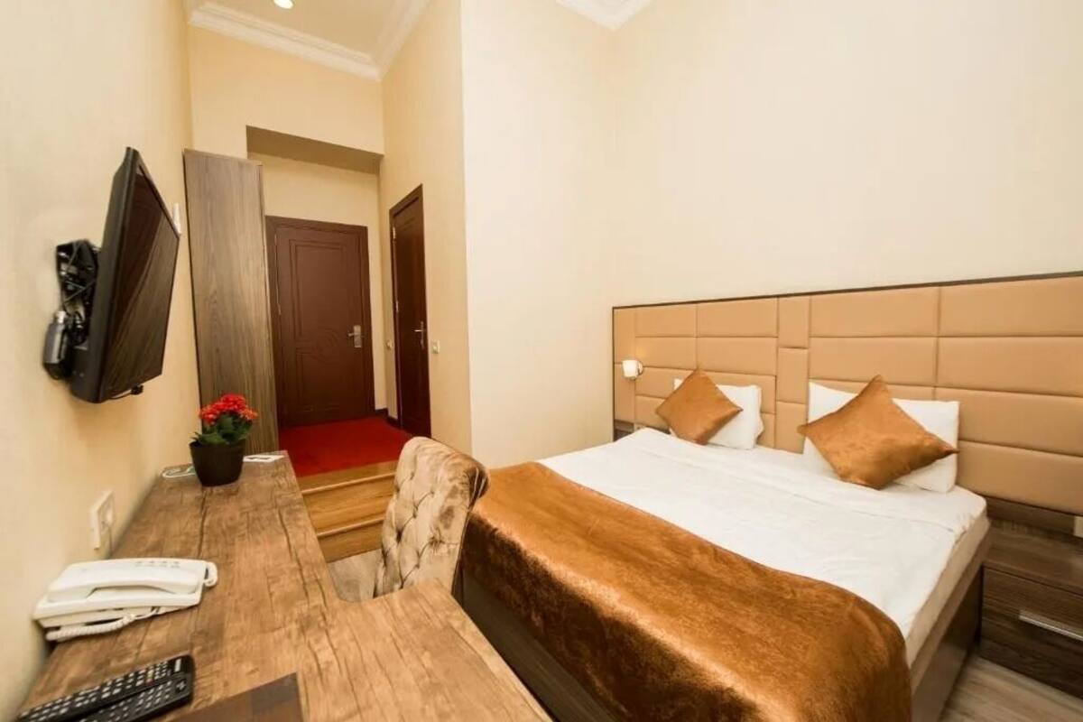 Ein Hotelzimmer mit einem Bett, einem Schreibtisch mit Telefon, einem an der Wand befestigten Fernseher und einer Tür zu einem weiteren Zimmer.