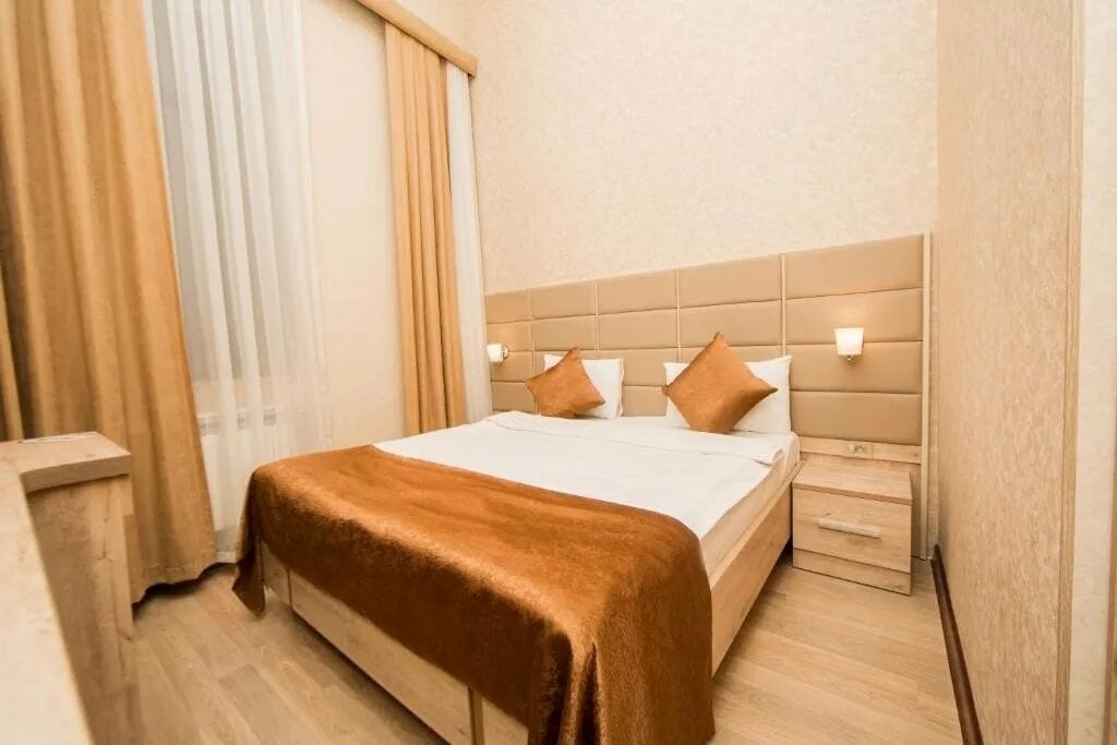 A neatly made bed with a brown blanket, a headboard with wall-mounted lights, and a wooden nightstand with a drawer.