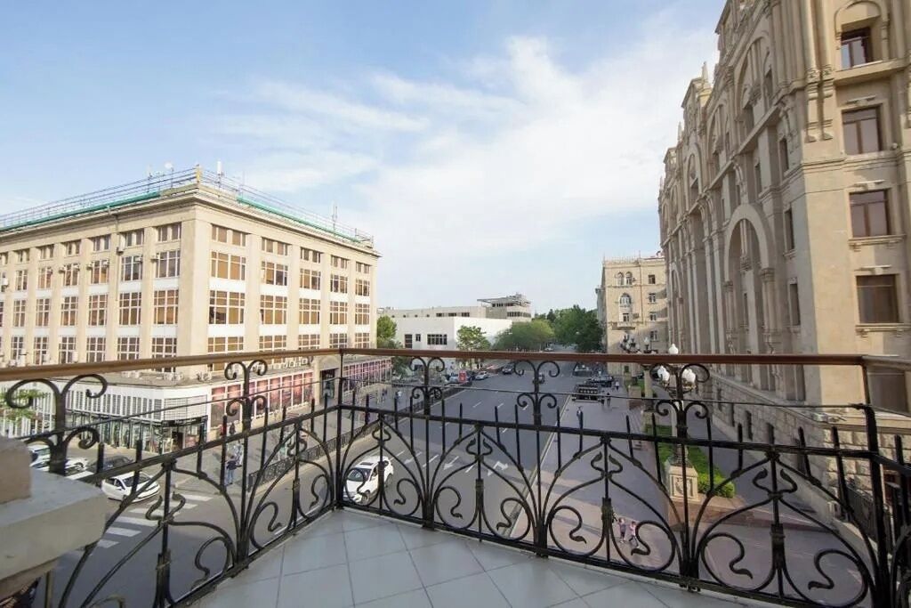 A balcony with a wrought iron railing overlooking a city street with buildings and a clear sky.