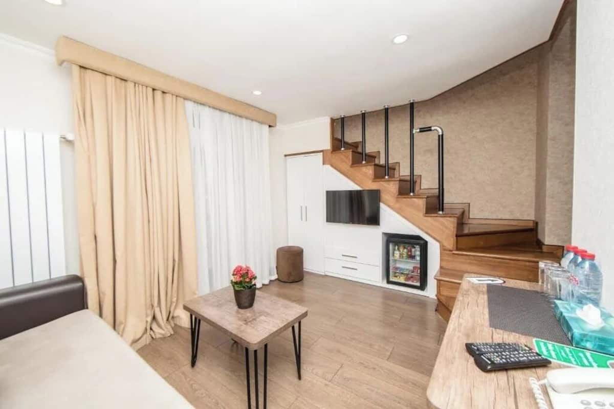 Ein modernes Wohnzimmer mit einer Holztreppe, einem Esstisch und einer Küchenzeile mit Kühlschrank.