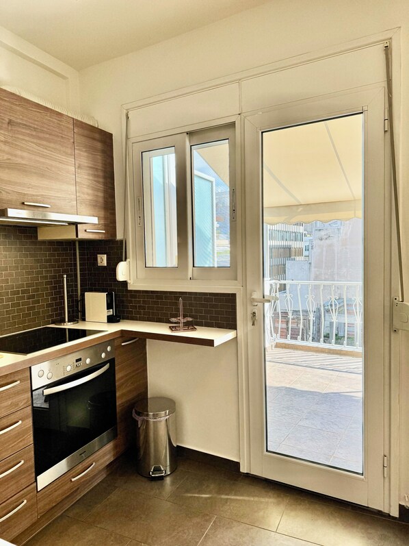 Eine moderne Küche mit Einbauofen, Dunstabzugshaube aus Edelstahl und Fenster mit Blick auf einen Balkon.