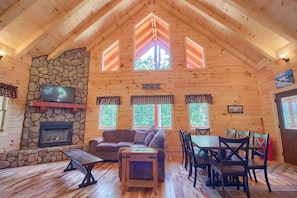 L’intérieur d’un chalet accueillant, avec une cheminée en pierre, des murs en bois, un canapé, une table et un coin repas.