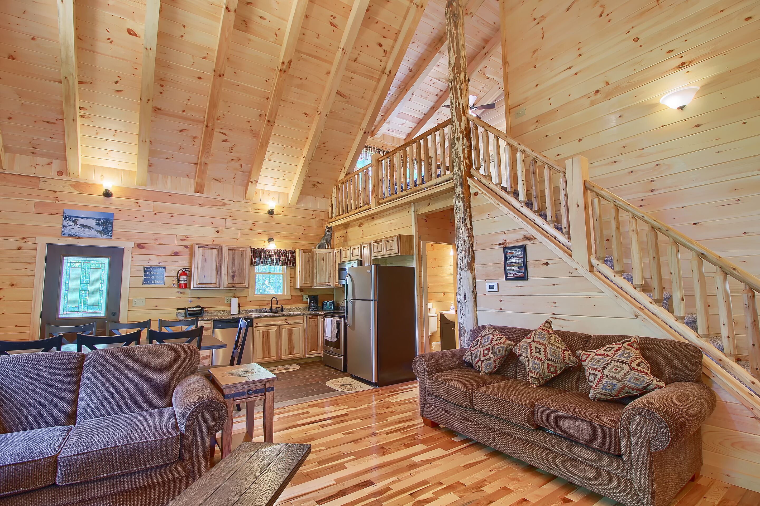 A cabin interior with a dining area, kitchen, and a staircase to an upper level.