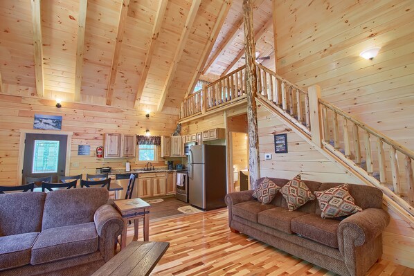 A cabin interior with a dining area, kitchen, and a staircase to an upper level.