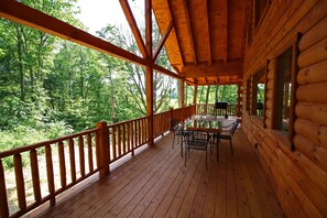 Eine Holzterrasse mit Tisch und Stühlen, umgeben von einem Geländer, mit Blick auf einen bewaldeten Bereich.