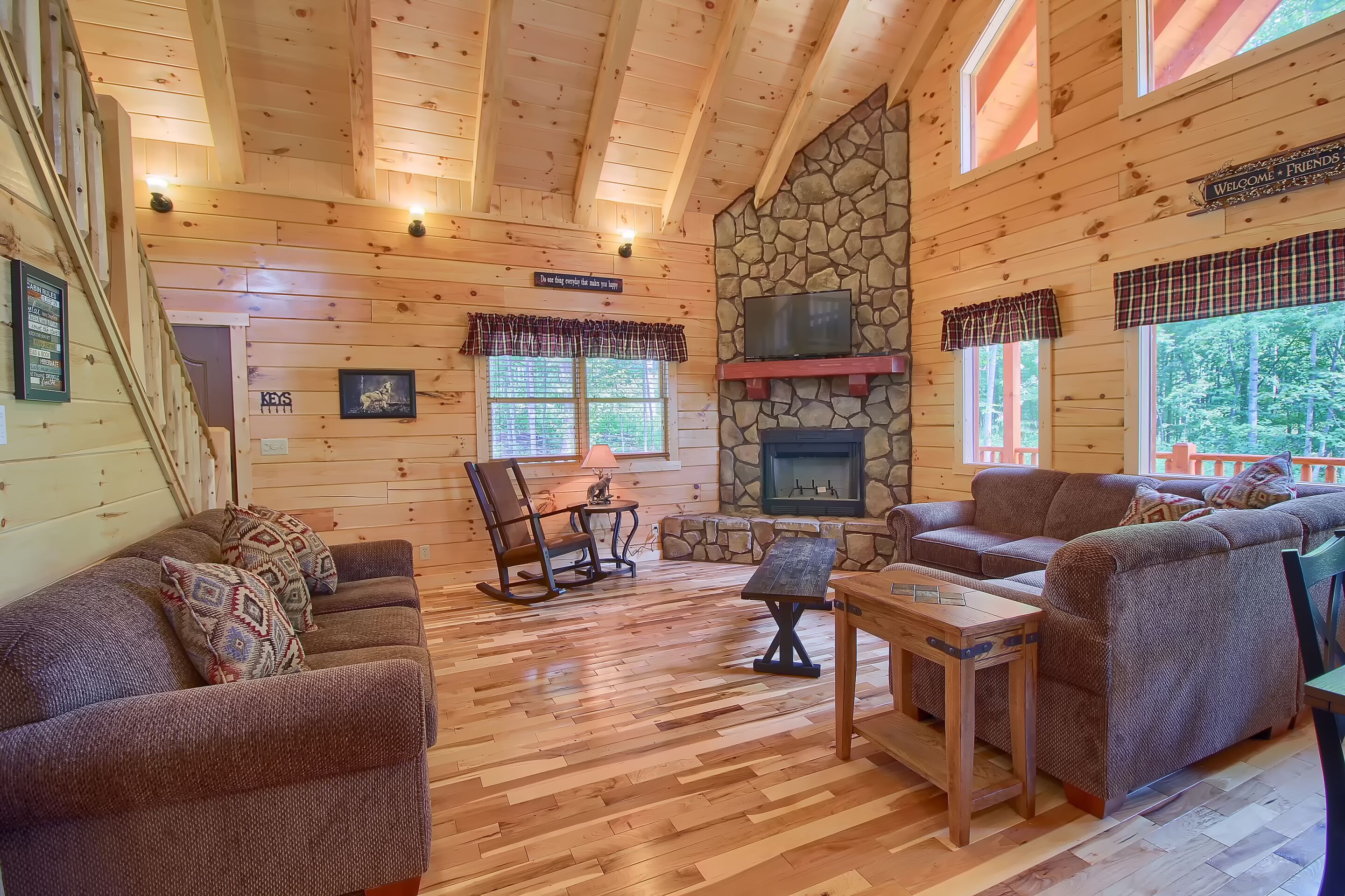 A cozy cabin interior with wooden walls, a stone fireplace, and a comfortable seating area.
