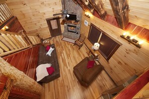 Een gezellig blokhutinterieur met een open haard, houten wanden, een bank en een eettafel.
