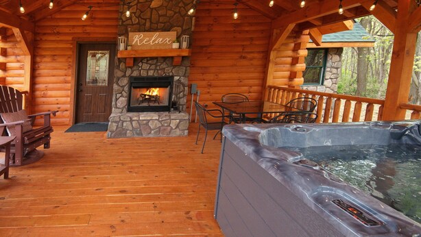 A log cabin with a stone fireplace, wooden deck, hot tub, and outdoor seating area. - Kalli's Luxury Retreat- Unique Couple's Cabin (Logan)