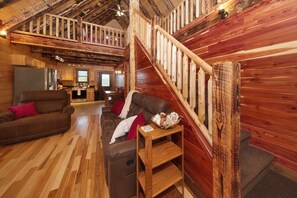 Un acogedor interior de cabaña con una escalera de madera, una sala de estar con un sofá y una mesa de centro, y una zona de cocina.