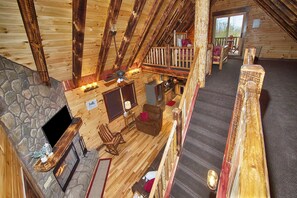 Una cabaña acogedora con chimenea de piedra, paredes de madera y un balcón con vistas panorámicas.