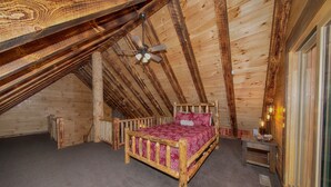 A wooden bedroom with a sloped ceiling, a wooden bed, a small bedside table, and a ceiling fan. - Kalli's Luxury Retreat- Unique Couple's Cabin (Logan)