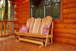 A wooden Adirondack chair with red and white patterned cushions on a wooden deck.
