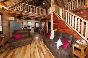 A spacious living area with a wooden staircase and a kitchen in the background.