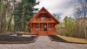 A wooden cabin with a balcony, surrounded by trees and a gravel driveway. - Kalli's Luxury Retreat- Unique Couple's Cabin (Logan)