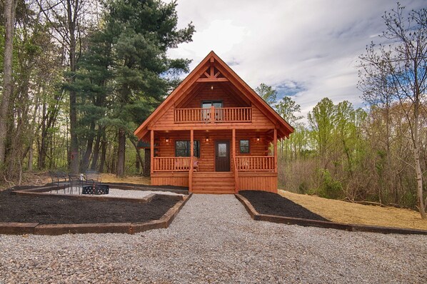 Une cabane en bois dotée d’un balcon, entourée d’arbres et bordée d’une allée en gravier.