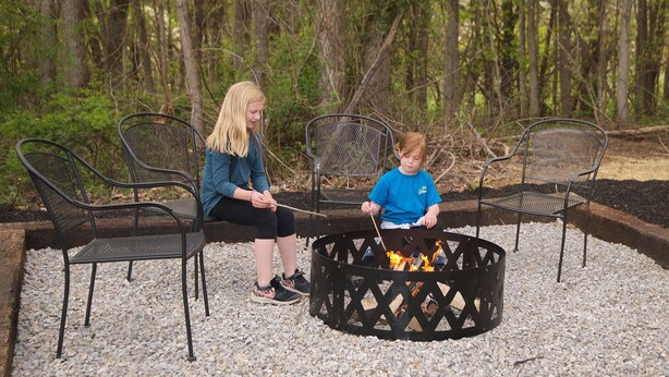 Two people sitting on metal chairs around a fire pit with a fire burning. - Kalli's Luxury Retreat- Unique Couple's Cabin (Logan)