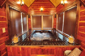 Interior de una cabaña de madera con jacuzzi, paredes de madera y dos ventanas con persianas.