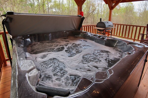 A hot tub with a wooden deck and a grill.