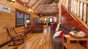 A cozy cabin interior with wooden walls, a loft bedroom, a dining area, and a kitchen. - Kalli's Luxury Retreat- Unique Couple's Cabin (Logan)