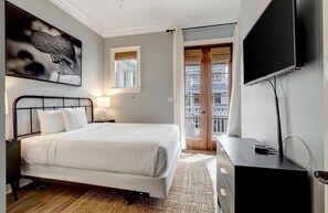 A hotel room with a bed, a television, a window with curtains, and a view of buildings outside.