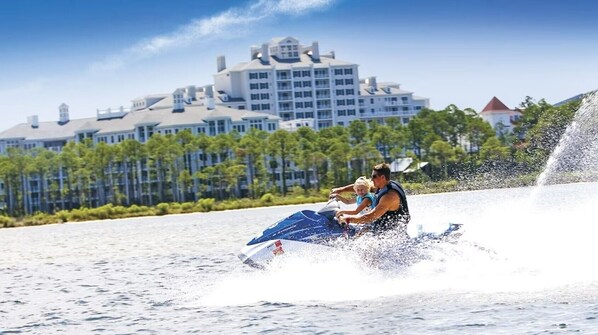 A water jet ski with two people, a large building with multiple floors in the background.