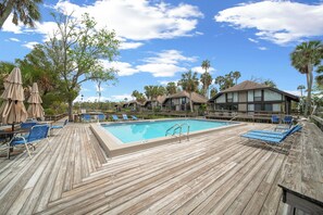 Eine Holzterrasse mit Schwimmbecken, blauen Liegestühlen und beschatteten Sonnenschirmen.
