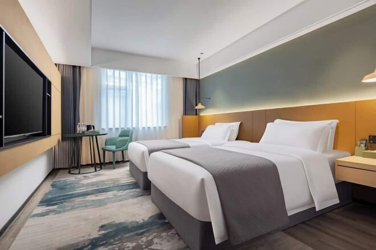 Quarto de hotel moderno com duas camas, uma televisão, uma mesinha e uma cadeira.