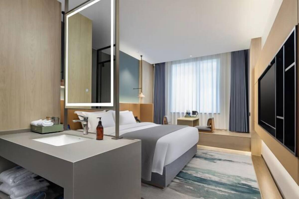Quarto de hotel moderno com uma cama grande, banheiro com toucador, espelho grande e televisão de tela plana.