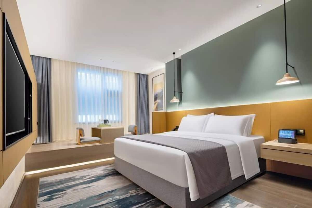 Quarto de hotel moderno com uma cama grande, mesas de cabeceira, televisão e vista para o exterior.