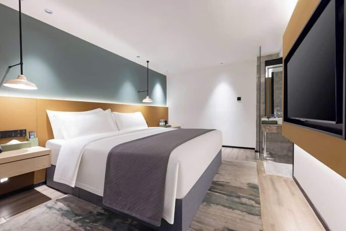 Quarto de hotel moderno com uma cama grande, mesas de cabeceira, uma TV de tela plana e um espelho grande.