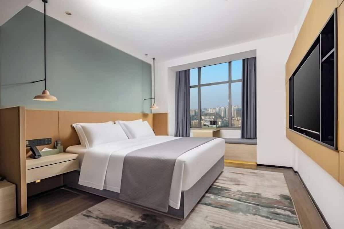 Quarto de hotel moderno com uma cama grande, uma escrivaninha, uma TV e vista para a cidade.