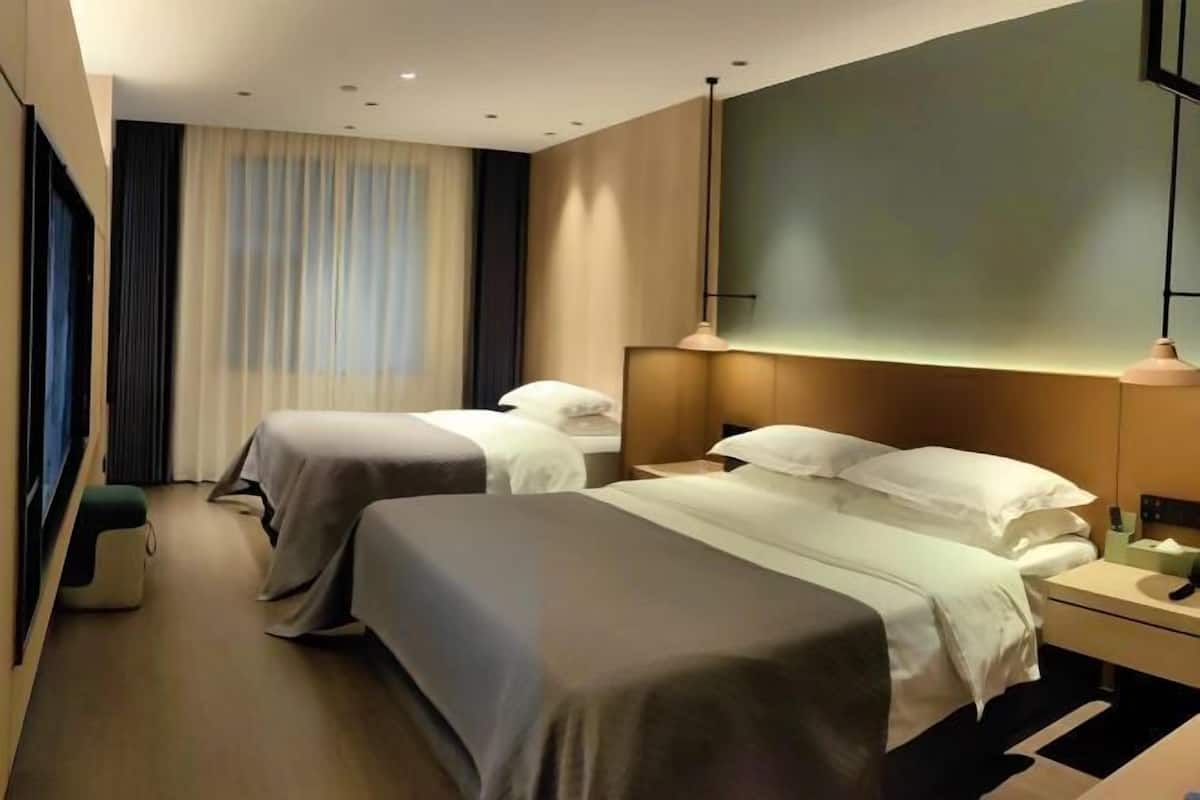 Quarto de hotel com duas camas, uma mesa de cabeceira, um abajur e uma janela grande com cortinas.
